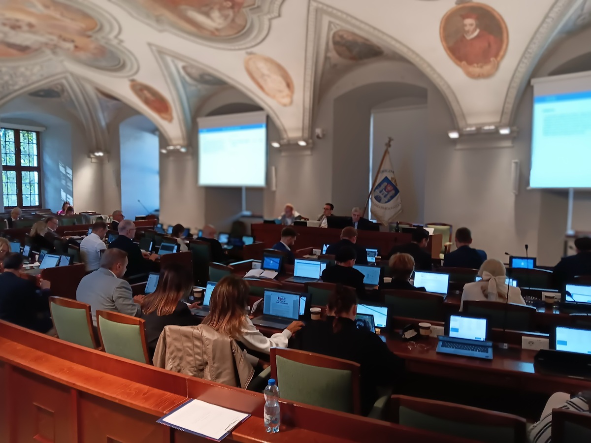 obrady na sali sesjyjnej, na stanowiskach z mikrofonami i monitorami siedzą radne i radni - grafika artykułu