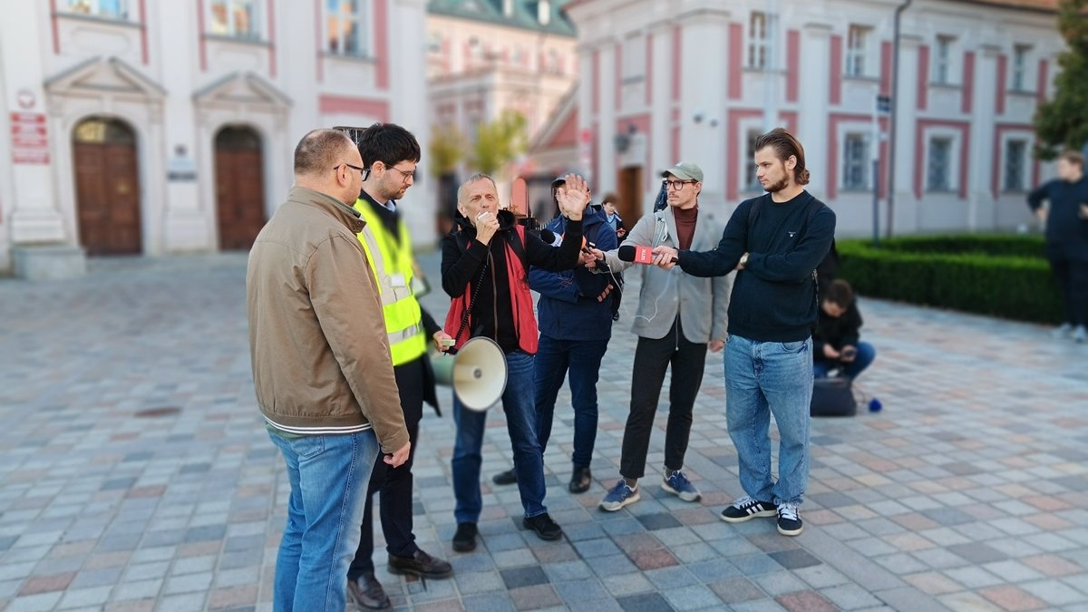 kilka osób stoi na placu z megafonem obok nich dziennkikarze z mikrofonami