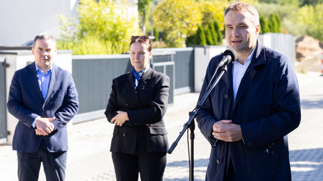 trzy osoby dwóch mężczyzn i kobieta stoją na ulicy jedna z tych osób mężczyzna stoi przy mikrofonie na stojaku