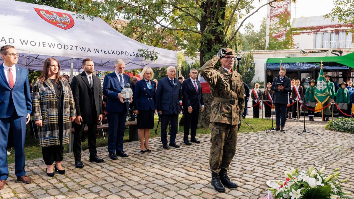 grupa osób kobiet i mężczyzn ustawiona w szergu przed pomnikiem przed nimi żołnierz salutuje ustawiony w kierunku pomnika