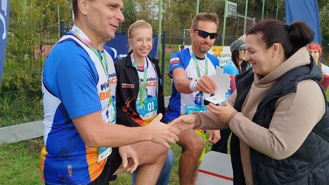 kobieta wręcza statuetkę uczestnikom biegu, którzy stoją na podium