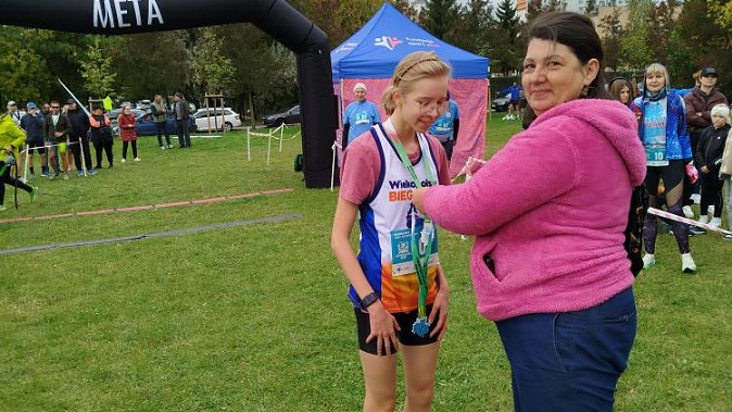 kobieta wręcza medal biegaczce, która dotarła na metę