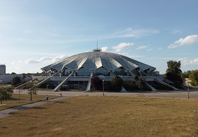 budowla przypominająca odwrócony spodek dookoła duży obszar trawy przy samej budowli ścieżka asfaltowa - grafika artykułu