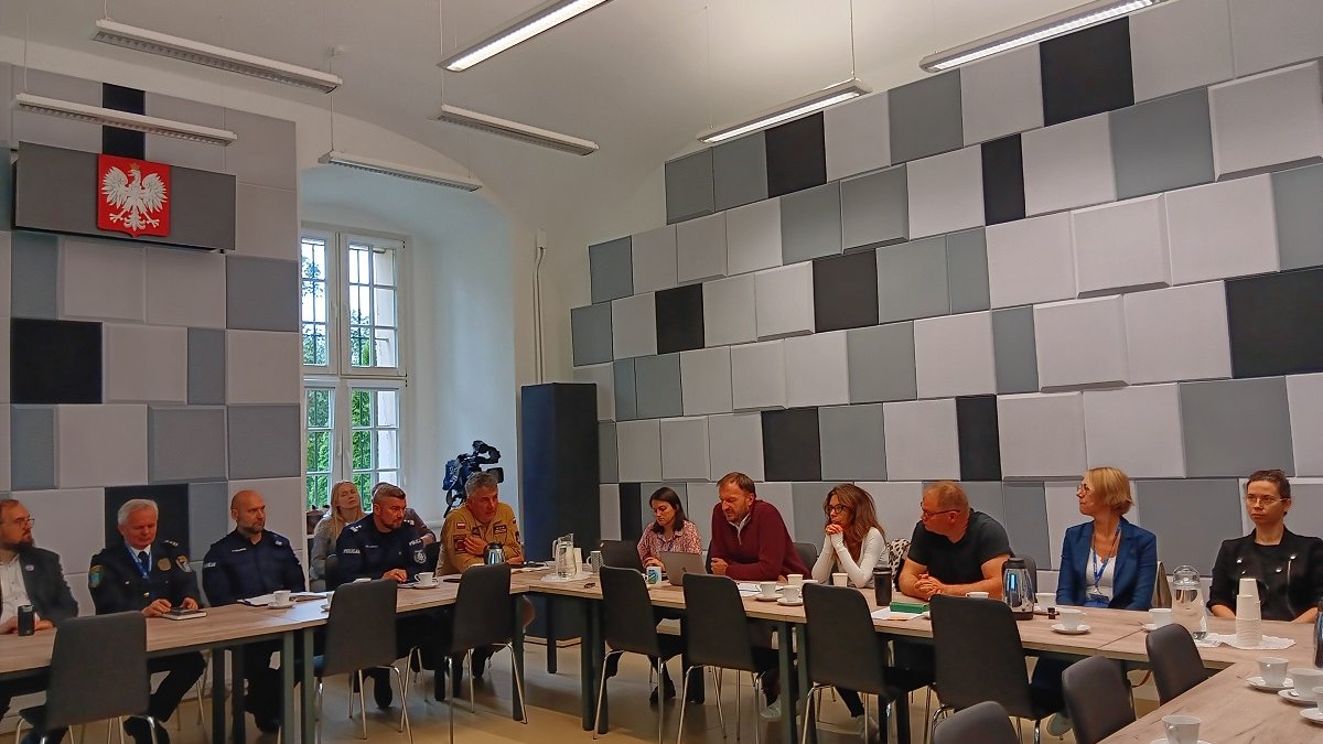 grupa około kilkunasti kobiet i mężczyzn sieci za stołem w sali konferencyjnej są wśród nich osoby w mundurach Policji Straży Pożarnej i Straży Miejskiej