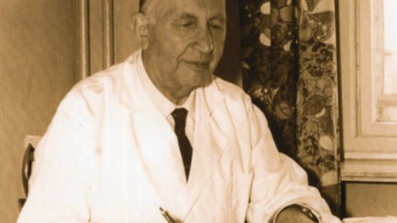 starszy mężczyzna w fartuchu lekarskim siedzi przy biurku - archiwalne zdjęcie Józefa Granatowicza