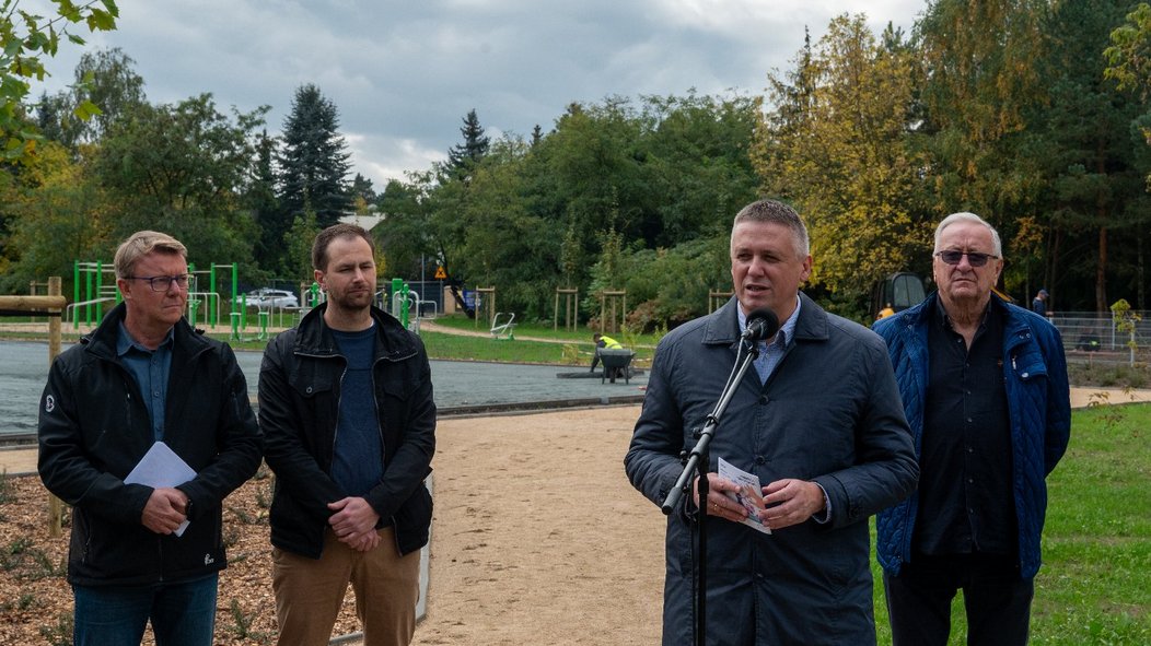 cztrerach mężczyzn uczetsniczy w konferencji prasowej stoja na tle kompleksu sportowo-rekreacyjnego