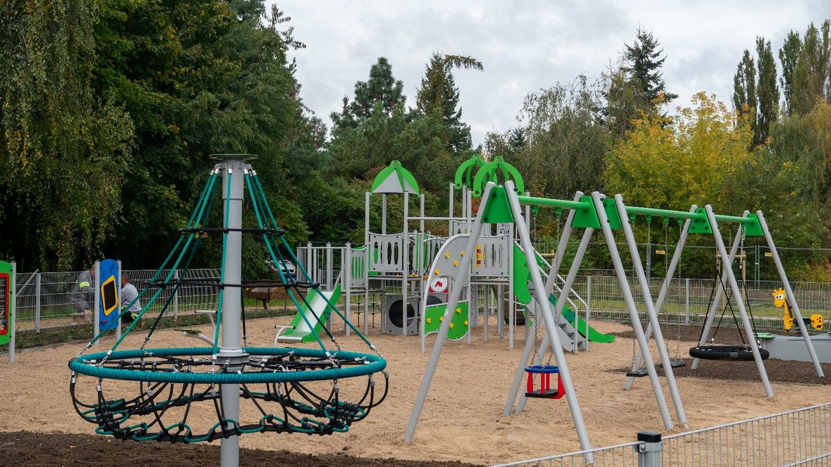 Osiedlowy komplekst sportowo-rekreacyjny z różnymi urządzeniami na piaszczystym podłożu otoczony drzewami