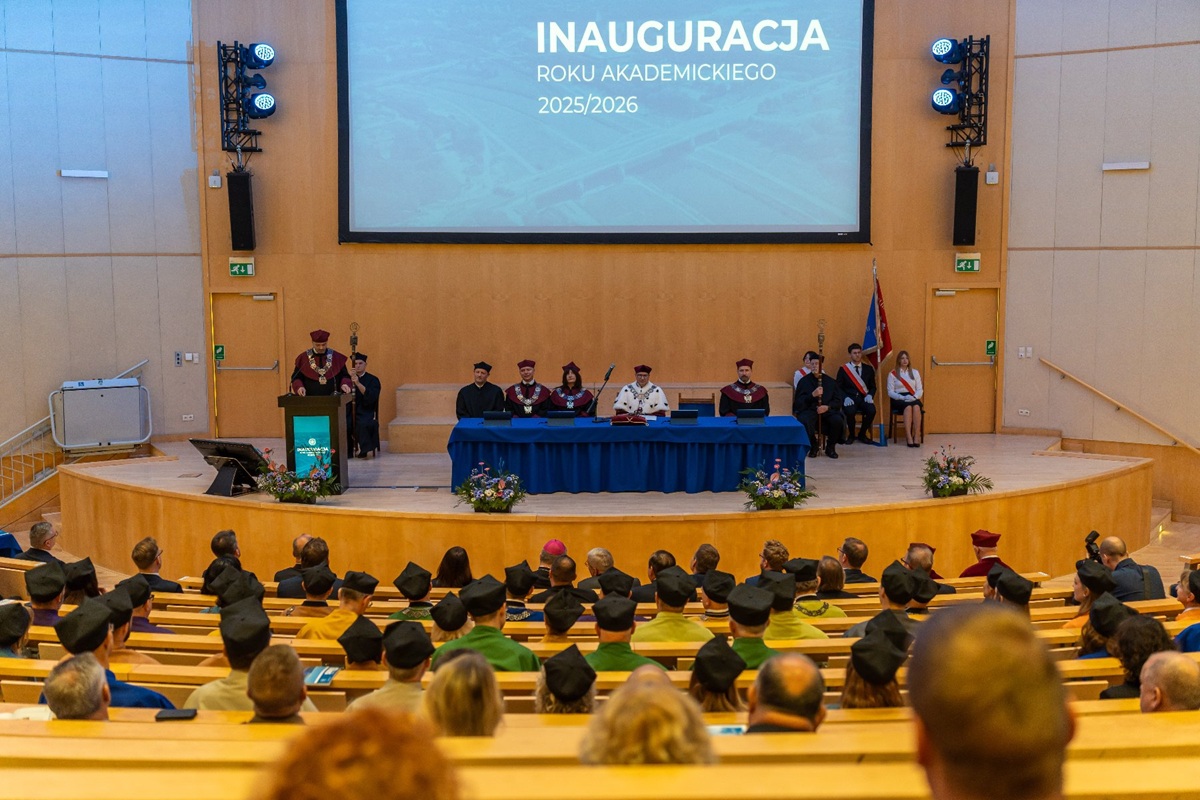 Duża aula stół prezydialny w nim osoby w strojach uroczystych władz uczelni na widowni inni uczestnicy uroczystości - grafika artykułu