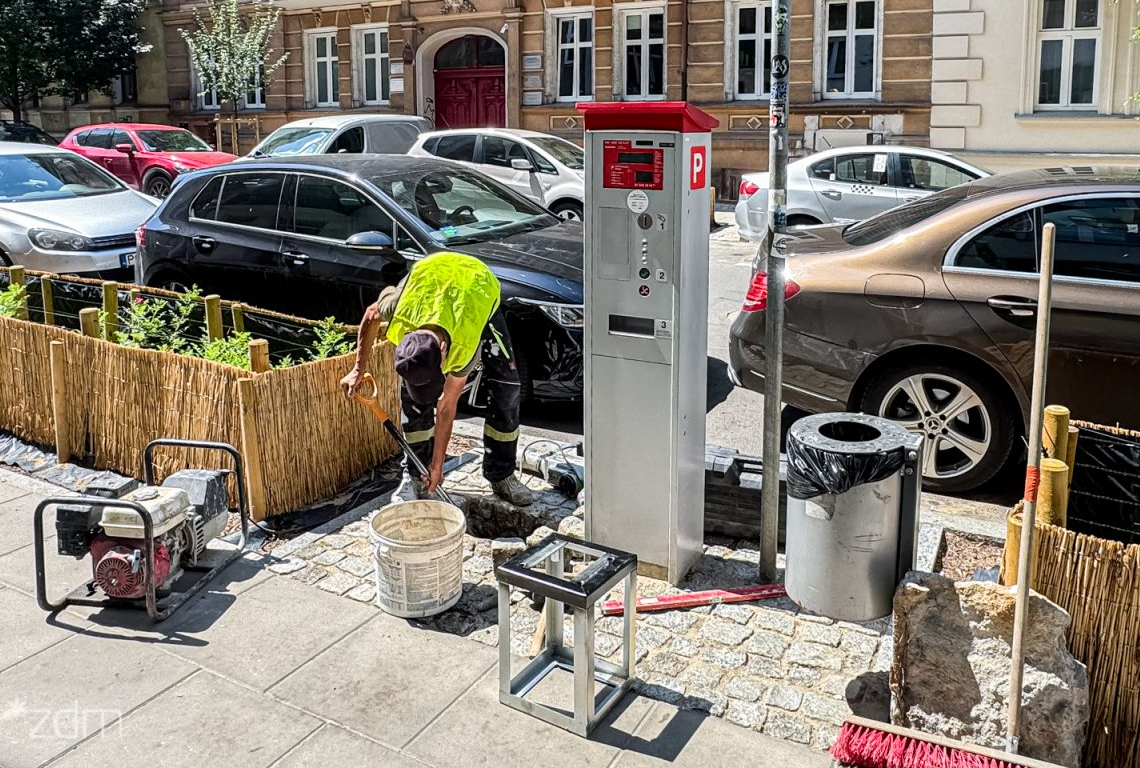 pracownik wykonuje prace związane z wykonaniem podstaw do montażu w chodniku nowych automatów parkingowych obok stoi stary automat - grafika artykułu