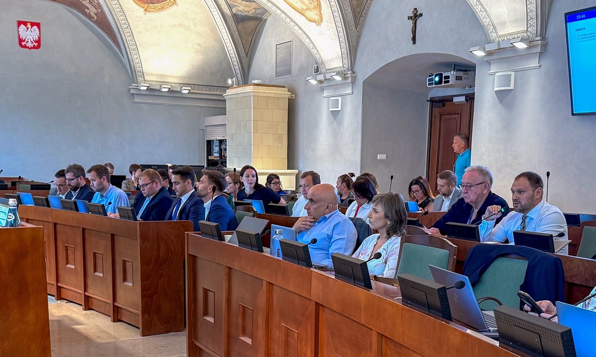 w zabytkowej z barwnymi freskami przy stanowiskach z mikrofonami i monitorami obradują radne i radni - grafika artykułu - grafika artykułu