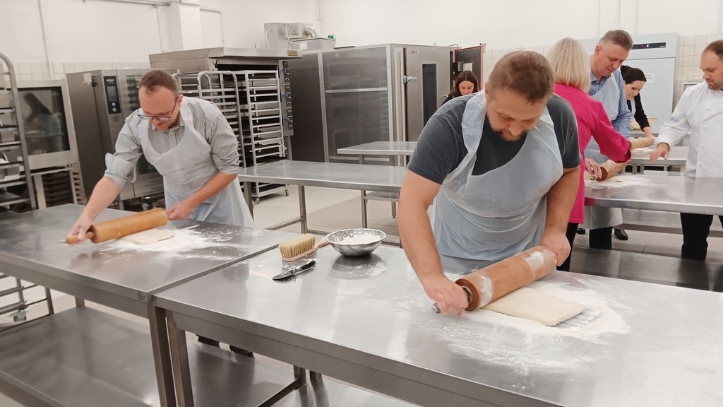 dwóch mężczyzn za stołem piekarniczym wałkuje ciasto
