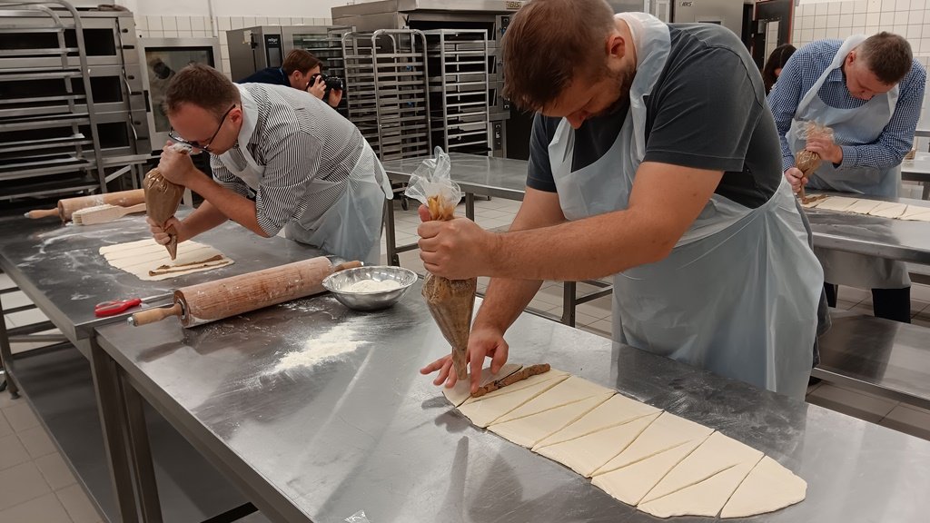 dwóch mężczyzn w fartuchach za stołem piekarniczym układa masę do przygotowanych fragmentów ciasta