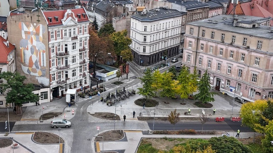 widok z dużej wysokości na skrzyżowanie ulic w śródmiejskiej zabudowie, między nimi skwer z drzewami