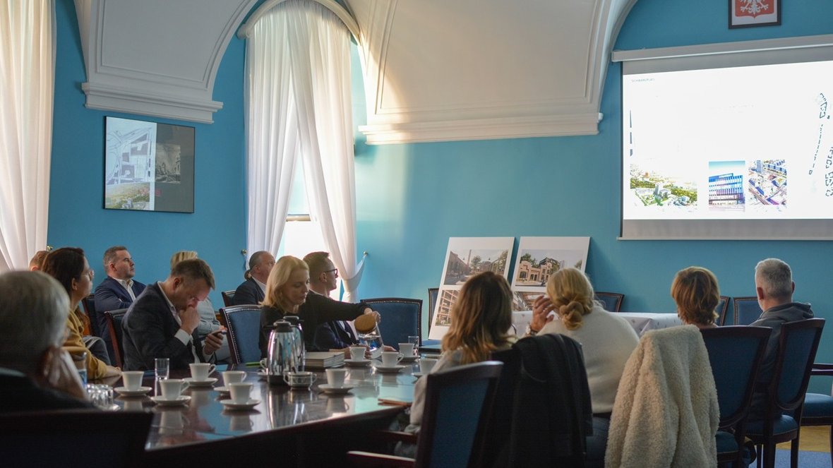 W sali konferencyjnej za stołem siedzi około kilkunastu osób, oglądają prezentację na dużym ekranie