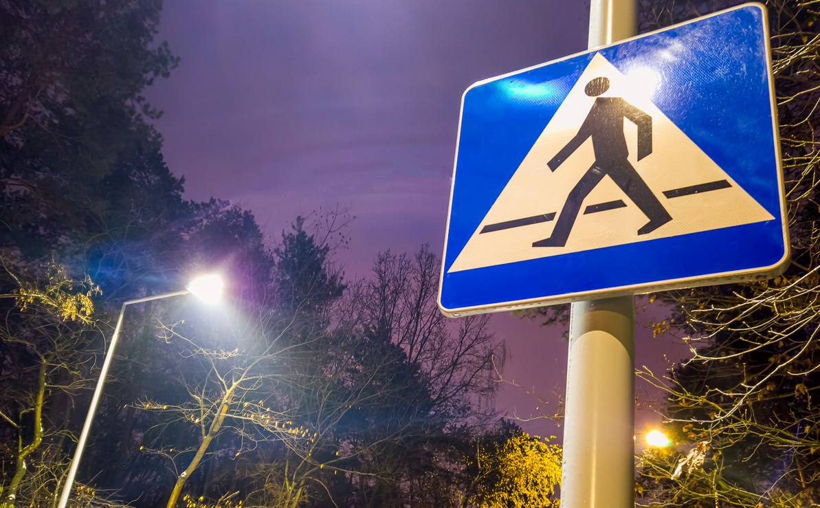 znak drogowy symbolizujący przejście dla pieszych, obok świecąca się latarnia uliczna - grafika artykułu - grafika artykułu