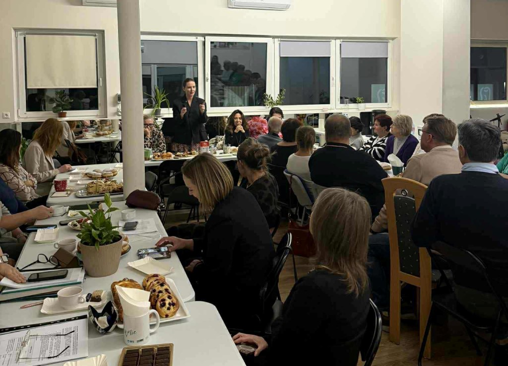 Posiedzenie Rodziny, Polityki Społecznej i Zdrowia w dniu 28 października 2025 r. spotkanie w osiedlowej świetlicy przy zastawionych stołach wiele osób w różnym wieku jedna osoba kobie stoi i przemawia do pozostałych