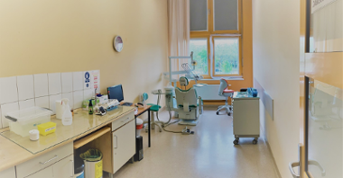 Zdjęcie przedstawia gabinet stomatologiczny. Widać na nim m.in. fotel dentystyczny oraz szafki.