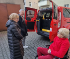 Zdjęcie przedstawia trzy osoby stojące obok czerwonego samochodu. Auto ma otwarte tylne drzwi.