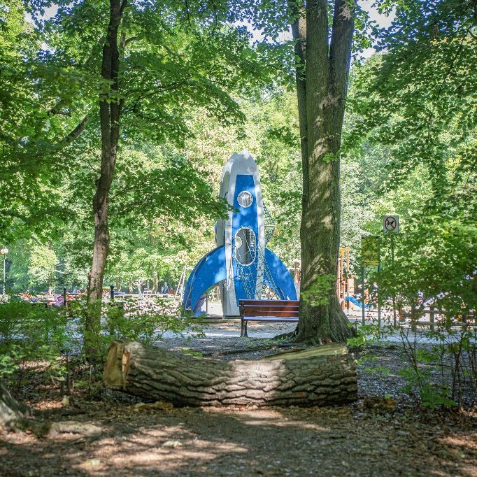 Niebieska rakieta na placu zabaw wśród drzew parkowych.