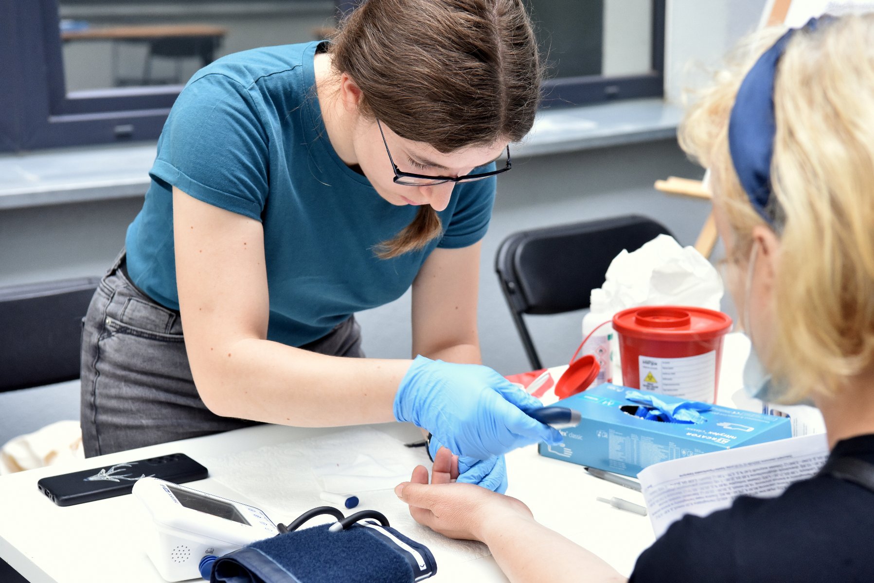 Dla chętnych przygotowano konsultacje dietetyczne, trychologiczne, farmaceutyczne i neurologopedyczne Na zdjęciu młoda kobieta pobierająca krew z palca innej kobiecie
