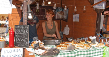 Zdjęcie przedstawia stoisko podczas jarmarku na Starym Rynku. Widać na nim panią sprzedającą bałkańskie przysmaki