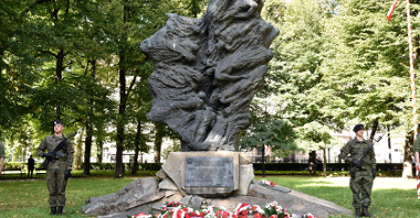 Zdjęcie przedstawia pomnik Ofiar Katynia i Sybiru, pod którym leżą wiązanki kwiatów.