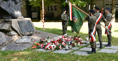 Zdjęcie przedstawia poczet sztandarowy i wiązanki kwiatów pod pomnikiem Ofiar Katynia i Sybiru.