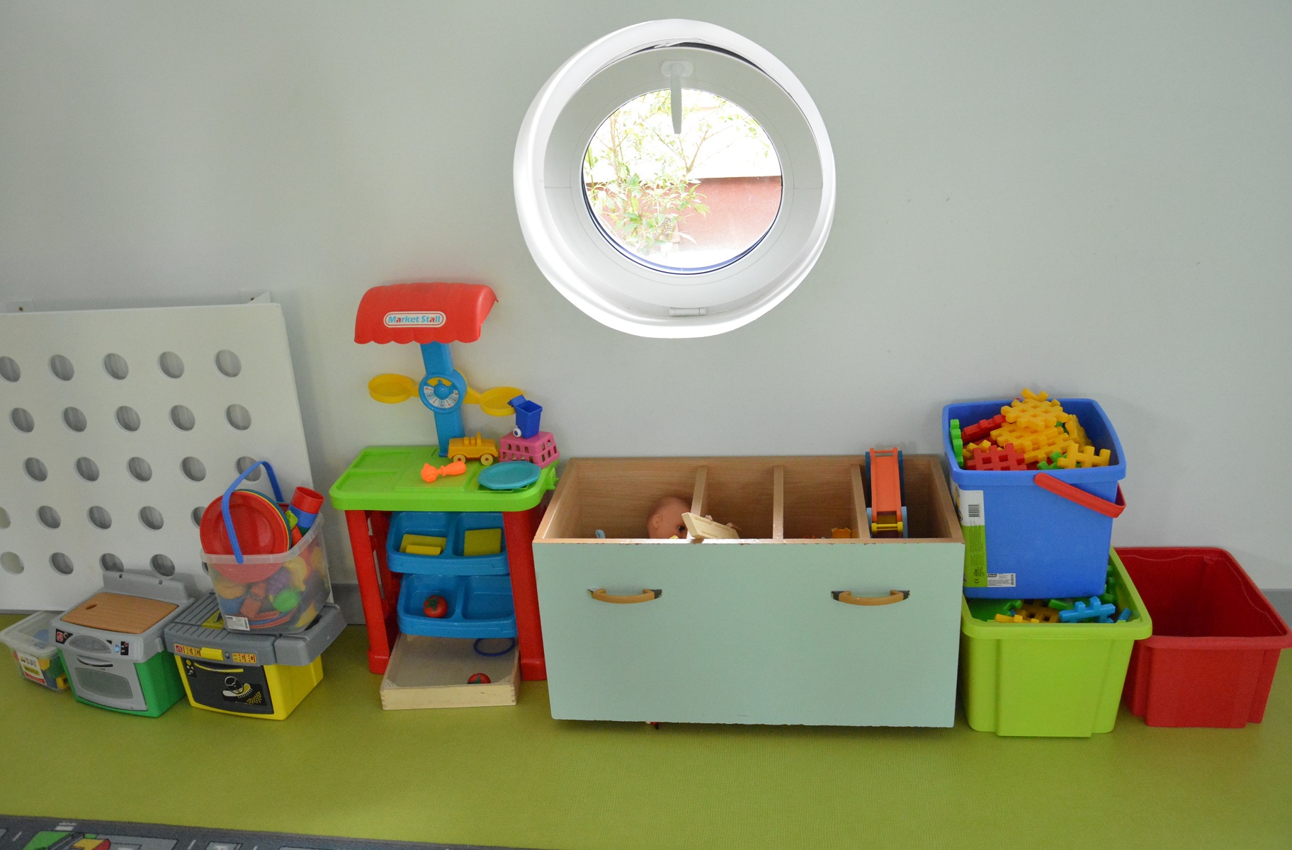 Na zdjęciu znajdują się przedszkolne zabawki stojące na zielonym stole - m.in. klocki w pudełkach, mini kuchenka. - grafika artykułu