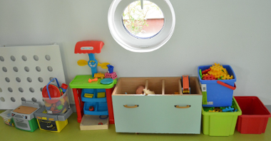 Na zdjęciu znajdują się przedszkolne zabawki stojące na zielonym stole - m.in. klocki w pudełkach, mini kuchenka.