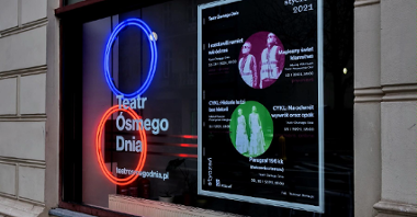 Zdjęcie przedstawia wejście do Teatru Ósmego Dnia. Na szybie okna znajduje się neon - czerwony i niebieski okrąg oraz plakat z repertuarem na styczeń.