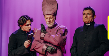 Zdjęcie przedstawia kadr ze spektaklu. Widać na nim biskupa i dwóch księży. Biskup stoi w środku.