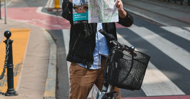 Mężczyzna na rowerze w centrum miasta, w rękach trzyma mapę