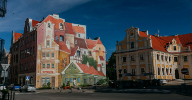 Zdjęcie przedstawia mural. Obraz na ścianie obrazuje budynki i robi wrażenie malowidła 3D.