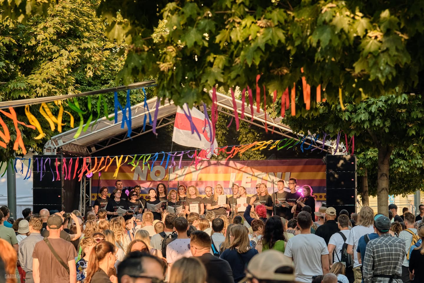 Święty Marcin zmieni się w przestrzeń dla pieszych pełną muzyki i kultury/ fot. Władysław Gardasz Zdjęcie przedstawia młodych artystów na scenie. Stoją tyłem do aparatu, a przodem do widowni, trzymają w ręce książki z nutami. Pod sceną stoi tłum ludzi. Scena znajduje się na zewnątrz.