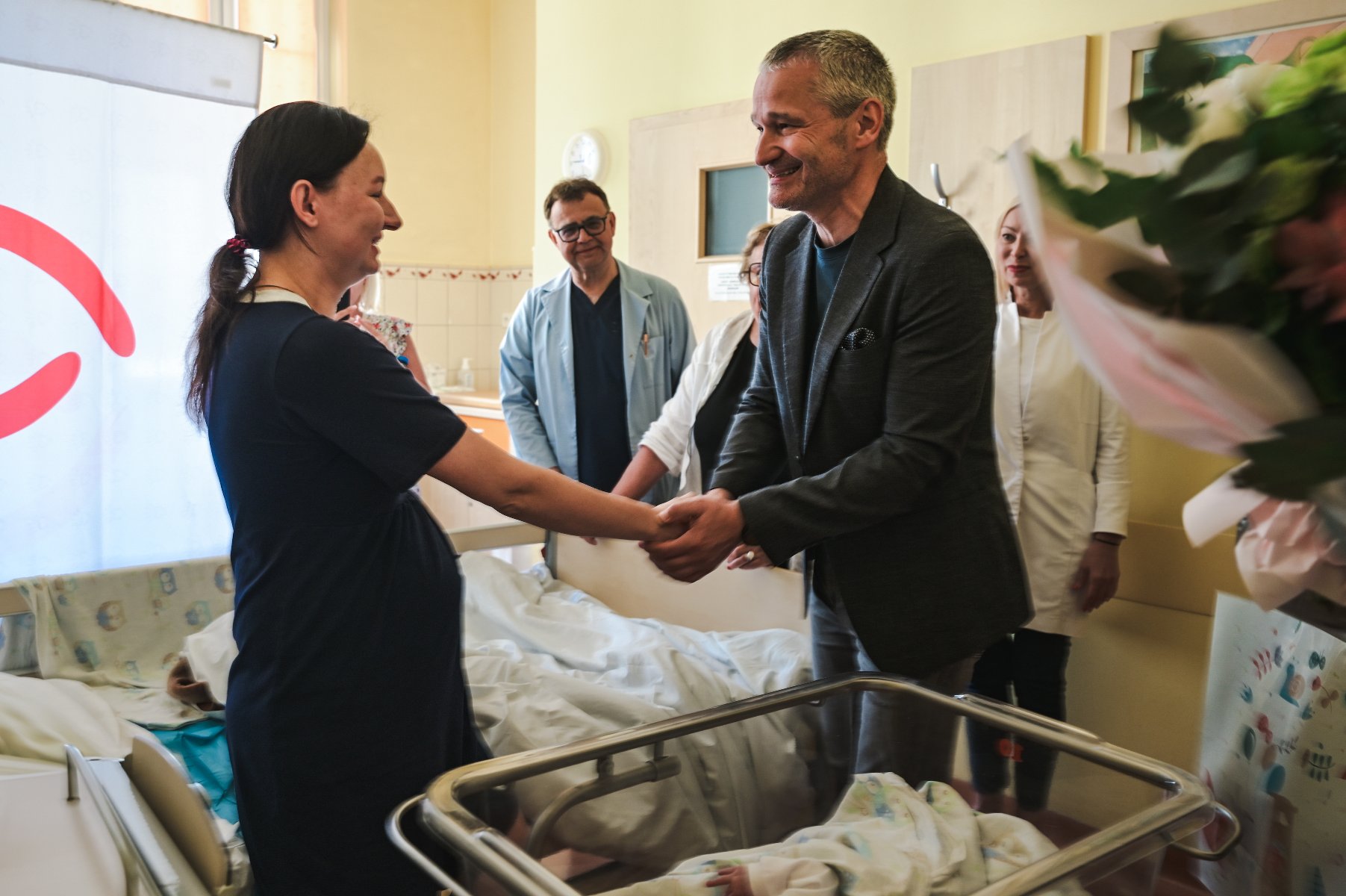 W miejskim szpitalu przyszedł na świat tysięczny noworodek. We wtorek Mariannę i jej mamę odwiedził zastępca prezydenta Jędrzej Solarski. Zdjęcie przedstawia wiceprezydenta ściskajacego rękę młodej kobiecie w szpitalnej sali. Za jego plecami stoją lekarze.