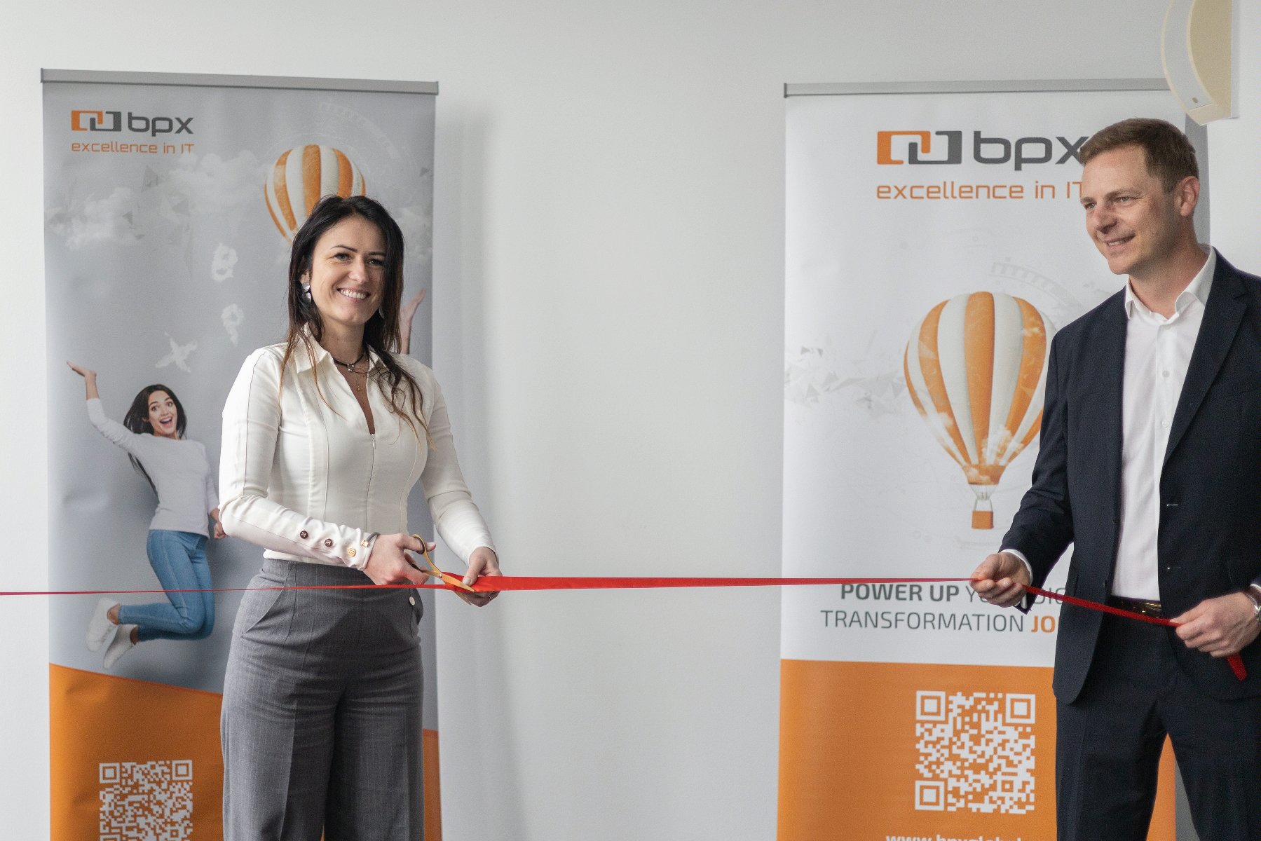 Obrazek przedstawia pracowników firmy BPX S.A. podczas uroczystego otwarcia nowego biura w Poznaniu. Dwie osoby przecinają uroczyście czerwoną wstęgę. - grafika artykułu
