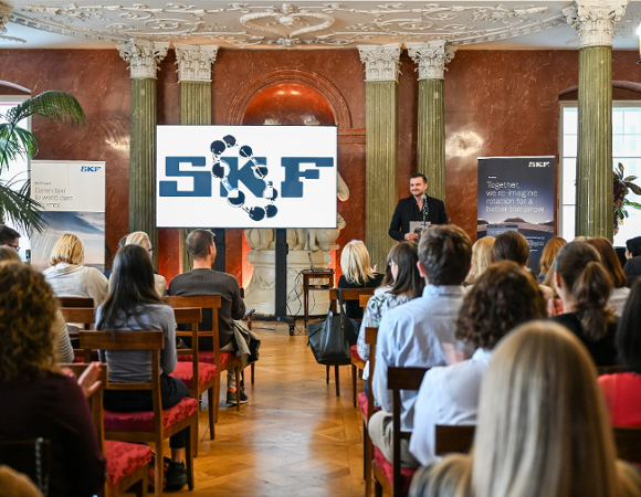 5-lecie SKF Business Center. Zdjęcie: Natalia Tomczak sala z siedzącymi uczestnikami wydarzenia. stojący prelegent. ekran z logiem SKF. roll-upy z misją SKF