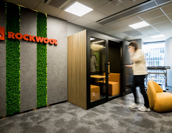 Poznański oddział ROCKWOOL świętuje 9. rocznicę Strefa ciszy na korytarzu biurowym. Na ścianie z pasem zieleni wisi logo ROCKWOOL.
