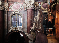 Old Town Organ Concerts, 2023, photograph: Dawid Stube The interior of the parish church. At the top, by the side organs, sits a musician, behind him stands his companion. On the balustrades stand beautiful figures of cherubs, on the walls around hang ornate paintings of the "Stations of the Cross".