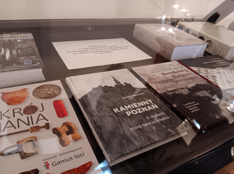 Książka "Kamienny Poznań. O skałach które tworzą miasto", Janusza Skoczylasa, wydana przez Wydawnictwo Miejskie Posnania, otrzymała nanagrodę w konkursie organizowanym przez PTPN gablota szklana, pod nią kilka książek w różnych formatach i różnych okładkach
