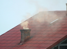 Na zdjęciu widać dymiący komin, który znajduje się na czerwonym dachu domu.