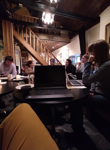 grupa ludzi przy rozmawiająca przy stole, na pierwszym planie laptop