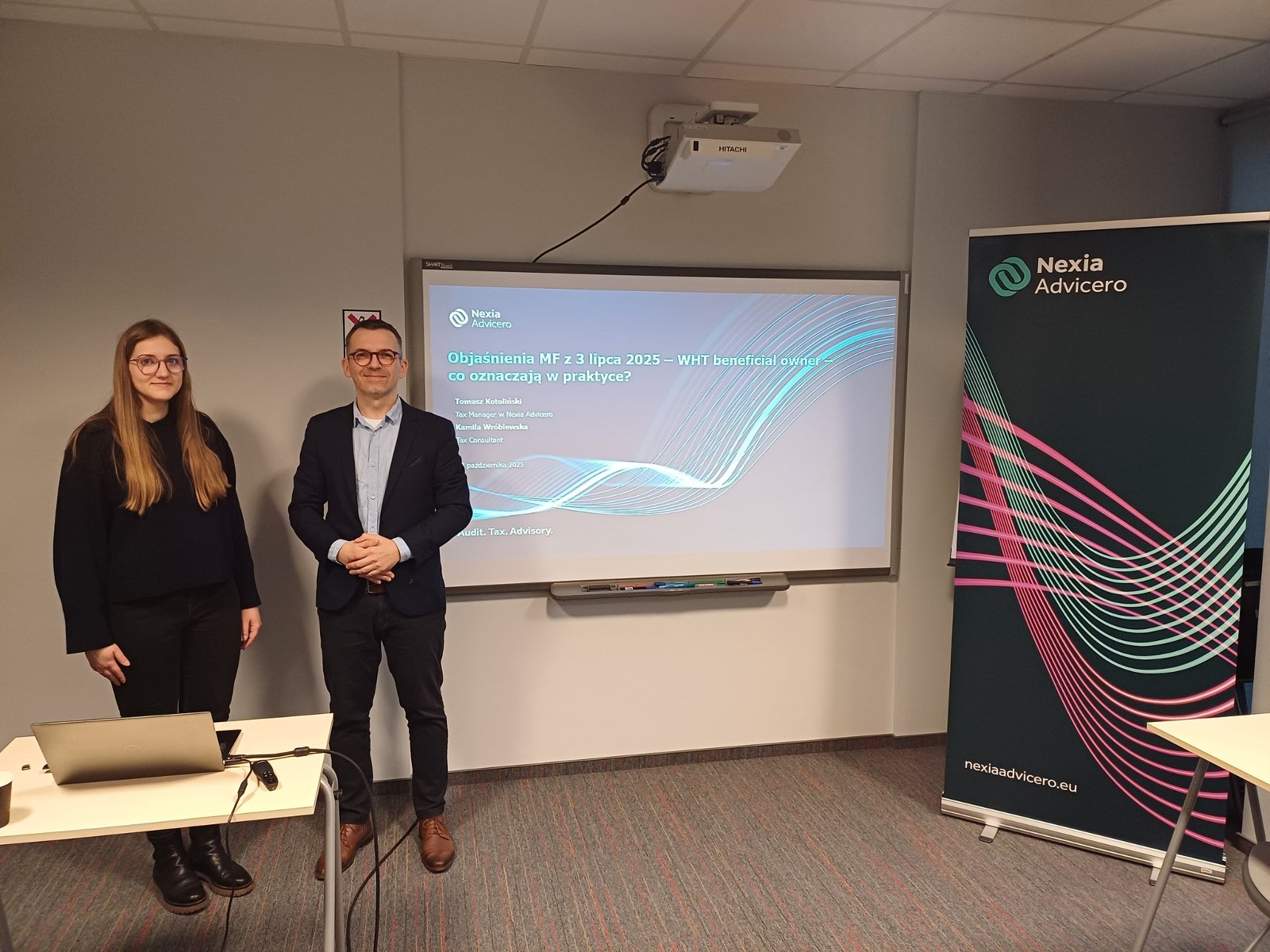 Szkolenie stacjonarne "Podatek u źródła - case study" w Poznań Biznes Partner Grafika ze szkolenia. Na zdjęciu prowadzący szkolenie i roll up Advicero Nexia