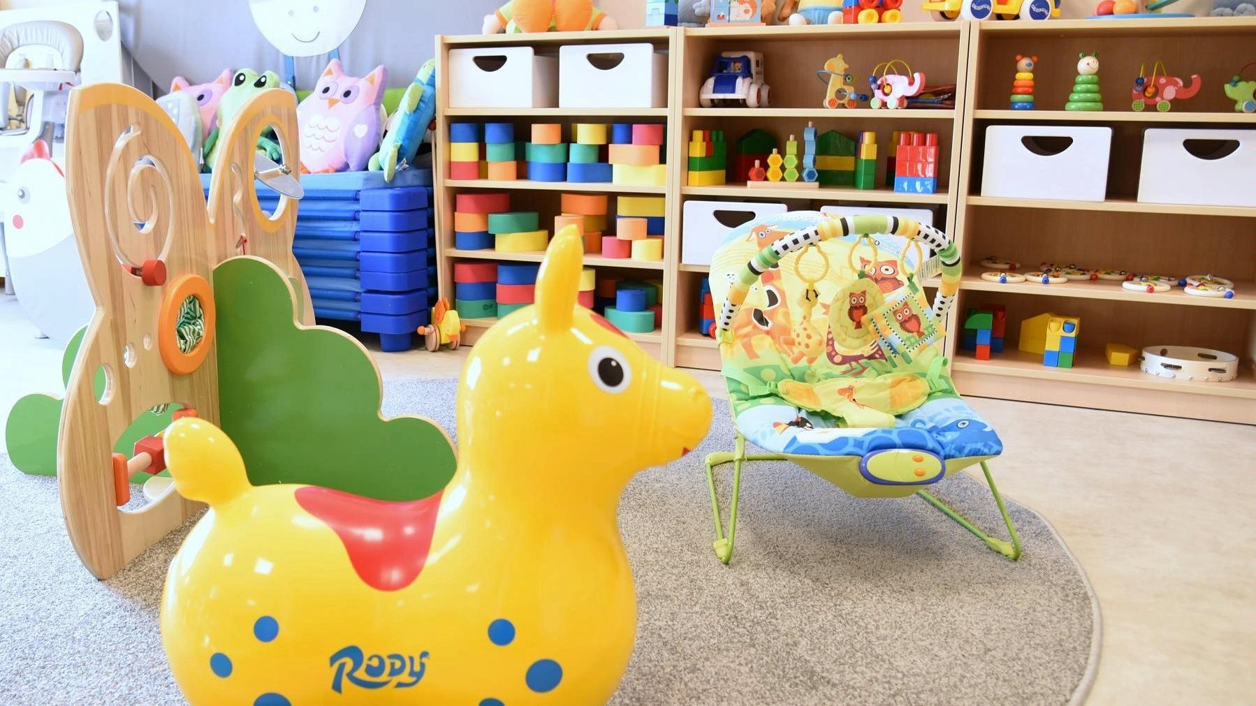 Zdjęcie przedstawia salę przedszkolną. Na pierwszym planie widać dziecięce krzesełko oraz dmuchaną zabawkę, w tle znajdują się półki z innymi zabawkami, m.in. klockami. - grafika artykułu