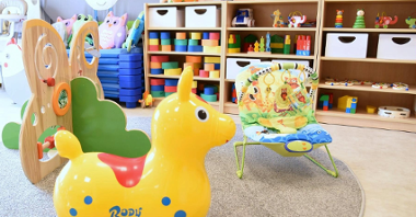 Zdjęcie przedstawia salę przedszkolną. Na pierwszym planie widać dziecięce krzesełko oraz dmuchaną zabawkę, w tle znajdują się półki z innymi zabawkami, m.in. klockami.