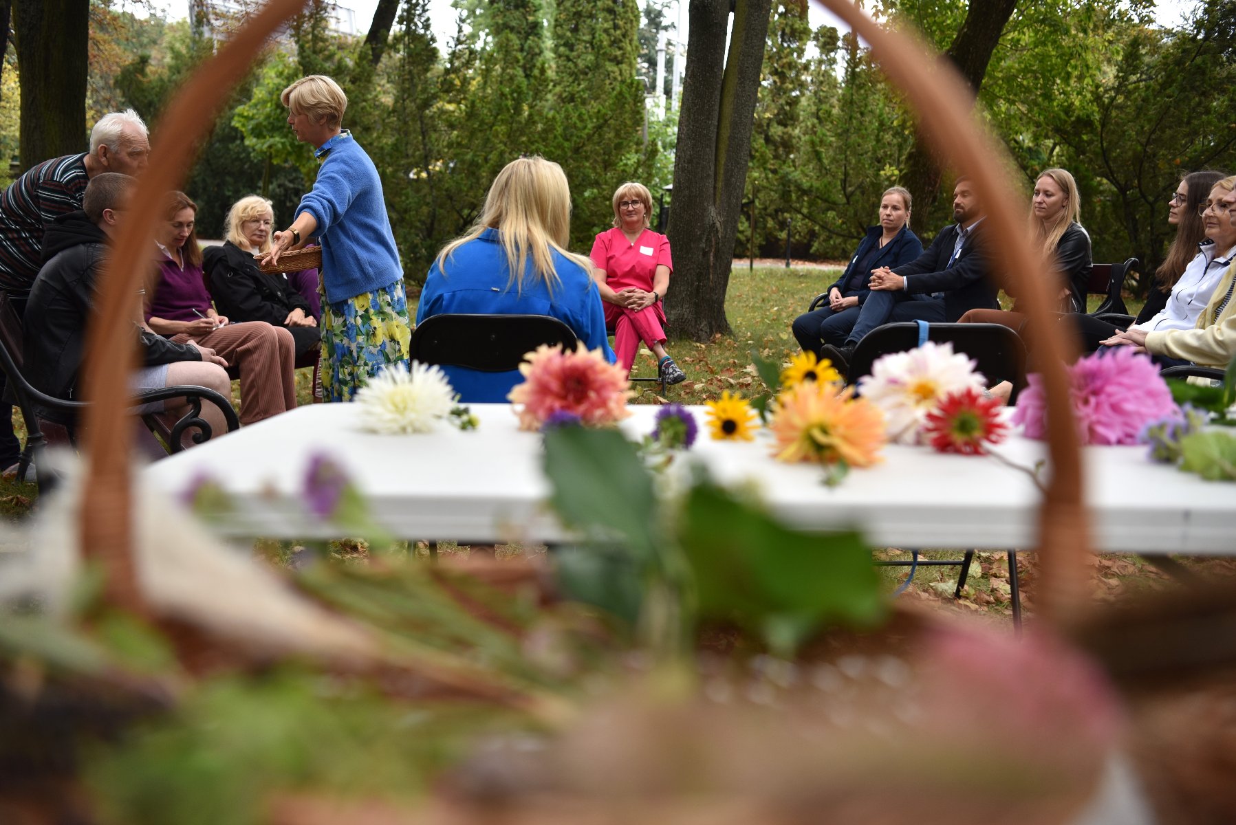 Program "Zielone Leczenie" jest realizowany przez Zarząd Zieleni Miejskiej przy współudziale poznańskich szpitali. Jednym z filarów projektu są bezpłatne warsztaty organizowane dla pacjentów. Zdjęcie przedstawia grupę ludzi siedzących na krzesłach wśród zieleni. Na pierwszym planie znajdują się kwiaty.