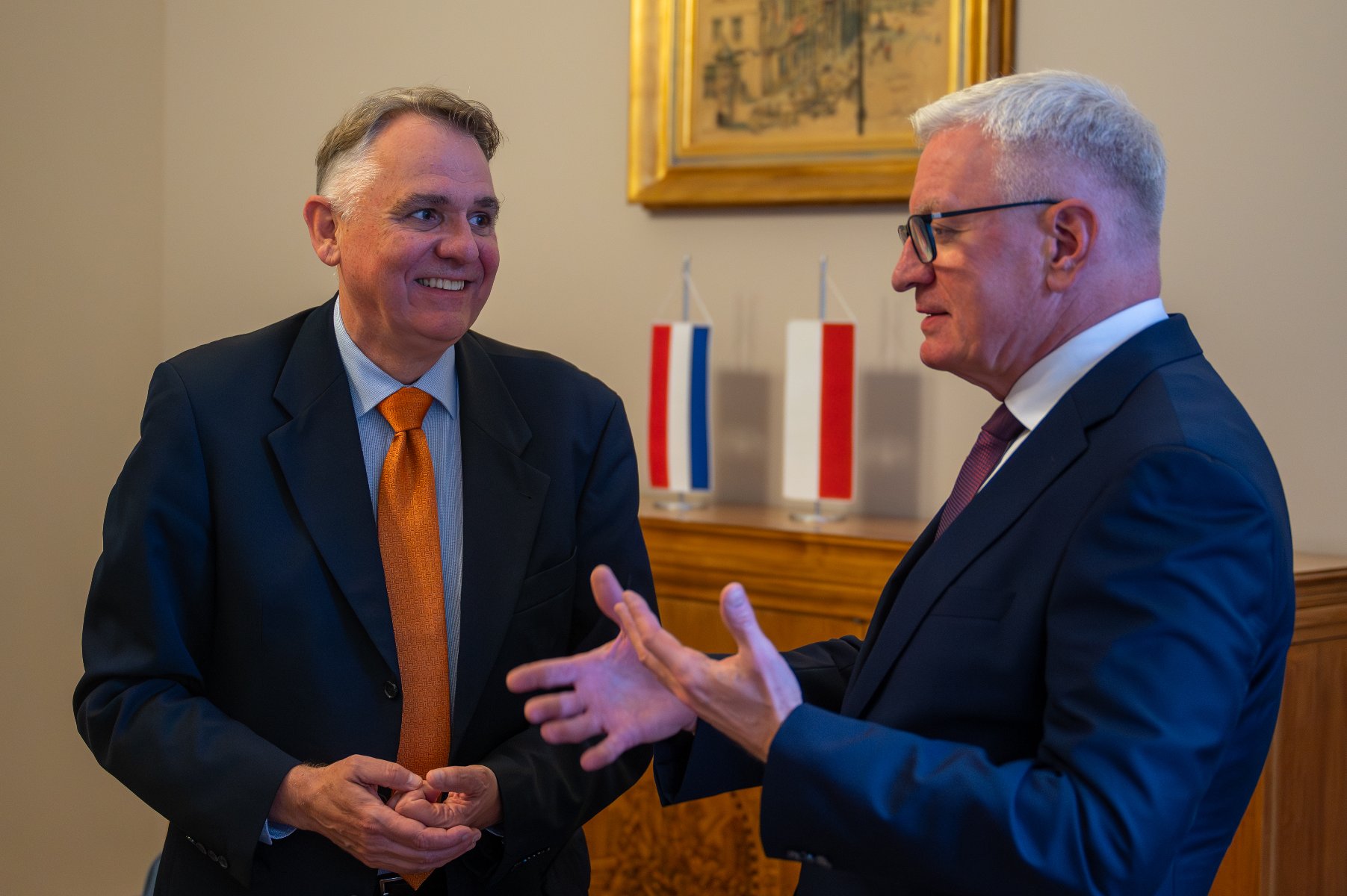 Johannes de Mol rozpoczął misję dyplomatyczną w naszym kraju we wrześniu 2024 roku Dwóch elegancko ubranych mężczyzn, w garniturach, rozmawia w pomieszczeniu. Mężczyzna po lewej, w pomarańczowym krawacie, uśmiecha się. Mężczyzna po prawej, w okularach, gestykuluje dłońmi. W tle widać dwie małe flagi: jedną biało-czerwono-niebieską i drugą biało-czerwoną.
