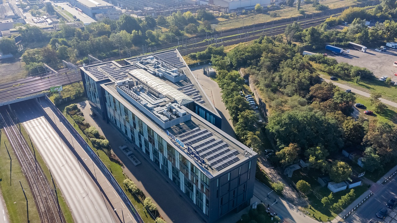 Widok w lotu ptaka na biurowiec Skalar Office Center Zdjęcie zostało zrobione z lotu ptaka. W środku kadru znajduje się biurowiec Skalar Office Center widoczny od góry. Za budynkiem widać tory kolejowe. Z lewej strony widać ulicę Hetmańską oraz tory tramwajowe. Z prawej strony budynku widać zadrzewiony teren oraz plac parkingowy.