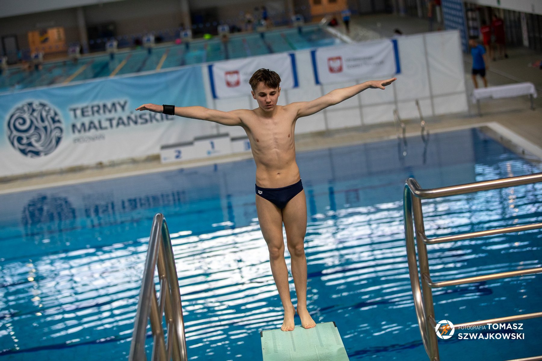 Skoki do wody w ramach Ogólnopolskiej Olimpiady Młodzieży w sportach letnich, fot. Tomasz Szwajkowski Skoki do wody w ramach Ogólnopolskiej Olimpiady Młodzieży w sportach letnich, fot. Tomasz Szwajkowski - mężczyzna stoi tyłem na pomoście przed skokiem do wody na pływalni. W tle widać pływalnię