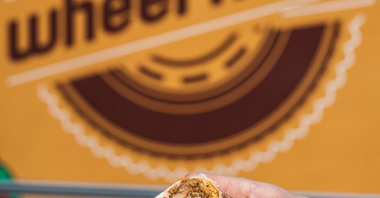 Przekrojone burrito trzymane w dłoniach. W tle logo "Wheal Meal".